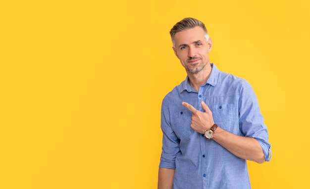 Homme d'âge mûr souriant avec montre-bracelet doigt pointé sur fond jaune copie espace heures d'ouverture