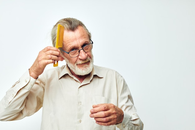 Homme âgé peignant ses cheveux avec un peigne jaune en studio sur fond gris