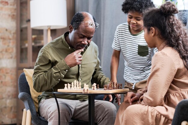 Homme âgé pensif regardant l'échiquier avec des figures en bois blanches et brunes