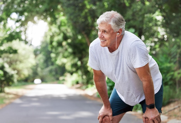 Homme âgé en plein air et repos avec des écouteurs de musique pour l'entraînement de course et l'entraînement sur la route pour le fitness Personne de sexe masculin âgée heureuse et fatiguée du cardio pour la santé et le bien-être avec audio pour la course