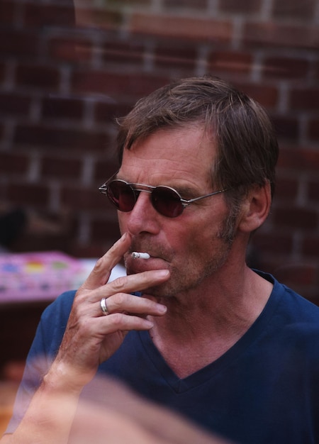 Homme âgé portant des lunettes de soleil tout en fumant une cigarette à l'extérieur