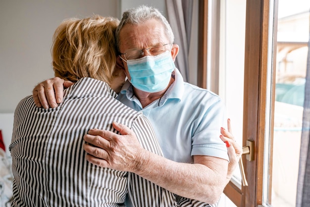 Un homme âgé portant un masque de protection avec les yeux fermés et embrassant sa femme Un couple âgé amoureux