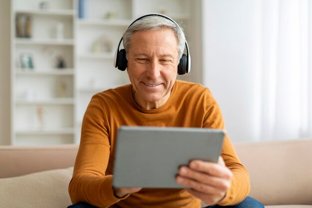 Homme âgé positif utilisant une tablette numérique et des écouteurs à la maison