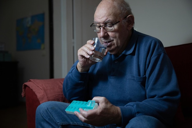 Un homme âgé prend des médicaments de son pilulier et boit de l'eau soins de santé domestiques