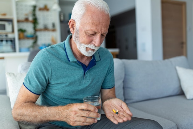 Un homme âgé prend une pilule avec un verre d'eau à la main Un homme mûr stressé buvant des antidépresseurs sédatifs Un homme se sent déprimé en prenant des drogues Des médicaments au travail