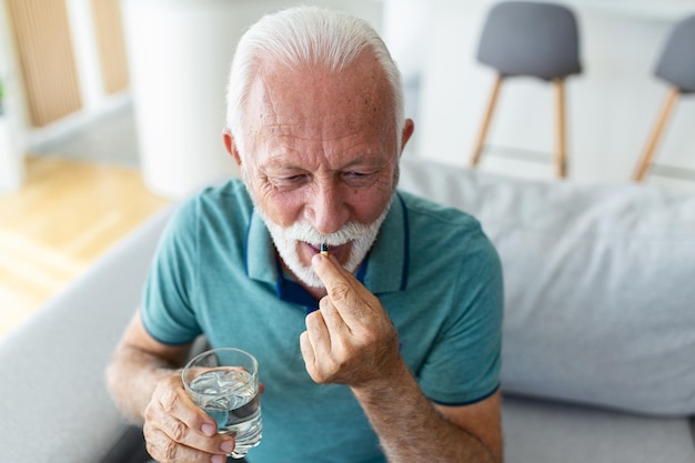 Un homme âgé prend une pilule avec un verre d'eau à la main Homme mûr stressé buvant des antidépresseurs sous sédation L'homme se sent déprimé en prenant des médicaments Médicaments au travail