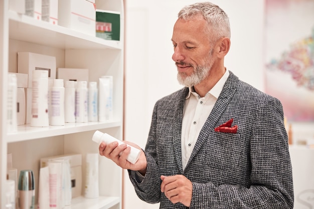 Homme âgé réfléchi regardant une petite bouteille blanche à la boutique