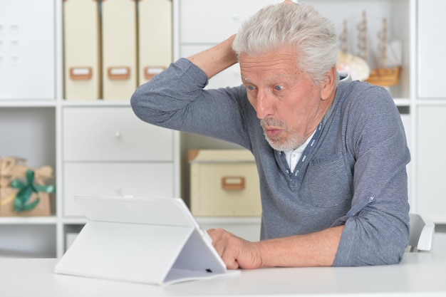 Homme âgé réfléchi avec tablette à la maison