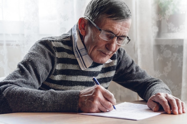 Un homme âgé résout le sudoku ou un jeu de mots croisés