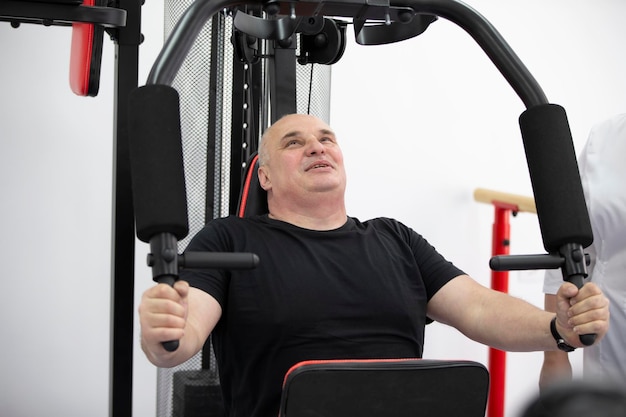 Photo un homme âgé s'entraîne sur une machine de sport en pompant les muscles de son bras