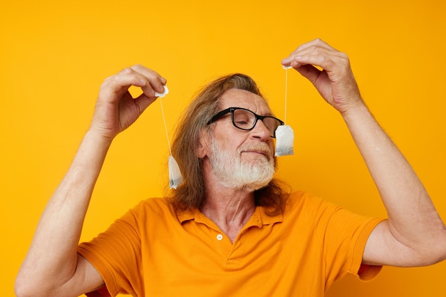 Homme âgé avec des sachets de thé fond jaune posant