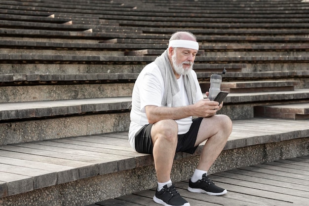 Homme âgé se reposant après l'extérieur à l'aide de son téléphone intelligent assis sur les escaliers à l'extérieur