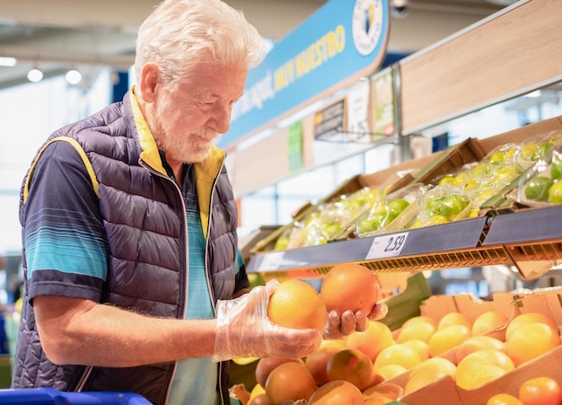 Photo homme âgé sélectionnant des pamplemousses ou des oranges au supermarché, achetant de l'épicerie, sélectionnant des fruits