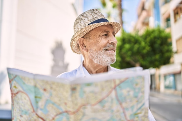 Homme âgé souriant confiant portant un chapeau d'été tenant une carte dans la rue