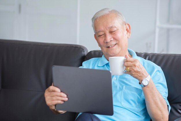 Homme âgé souriant lisant des nouvelles sur une tablette numérique Joyeux homme mature excité utilisant un ordinateur portable à la maison