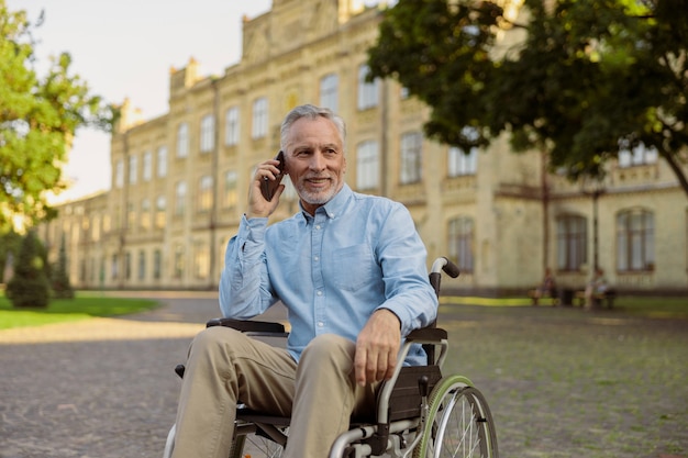 Homme âgé souriant récupérant un patient en fauteuil roulant en détournant les yeux tout en parlant au téléphone