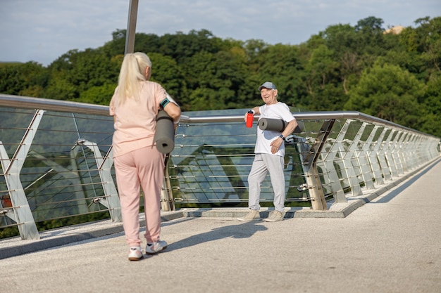 Un homme âgé souriant avec un tapis accueille une femme qui marche sur la passerelle