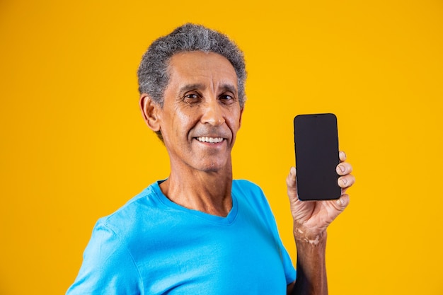 Homme âgé tenant un smartphone à écran blanc sur fond jaune.