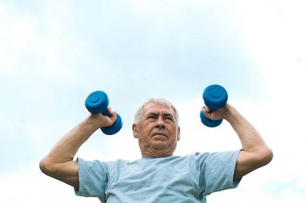 Homme âgé travaillant à l'extérieur Personne soulevant des haltères Vieil homme faisant de l'exercice contre le ciel bleu Mode de vie des personnes en bonne santé Entraînement sportif actif Sportif âgé plus âgé faisant des exercices de fitness Entraînement