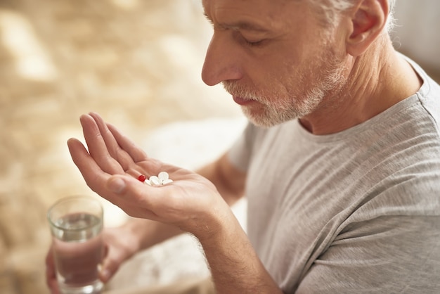 Homme âgé triste tenant des pilules et un verre d&#39;eau.