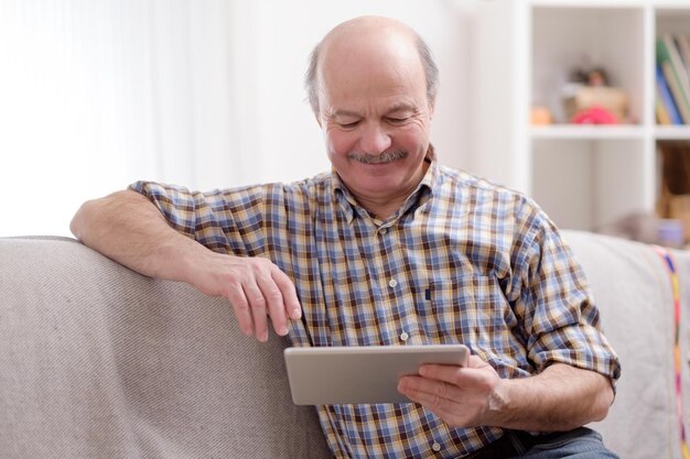 Homme âgé utilisant une tablette assis à la maison