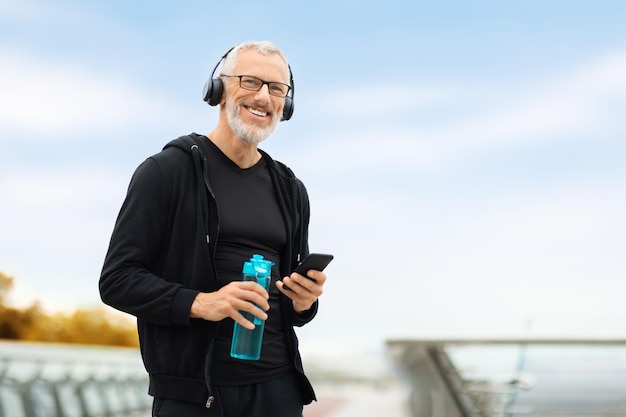 Homme âgé utilisant le téléphone tout en s'entraînant en plein air avec de l'eau potable