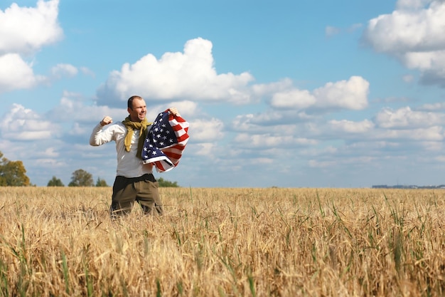 Homme agitant le drapeau américain debout dans le champ agricole de la ferme d'herbe, vacances, patriotisme, fierté, liberté, partis politiques, immigrant