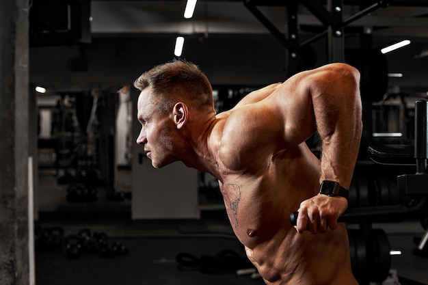 Un homme avec une agression sportive faisant pression sur les barres asymétriques dans une salle de sport, entraînant les muscles pectoraux et les triceps.