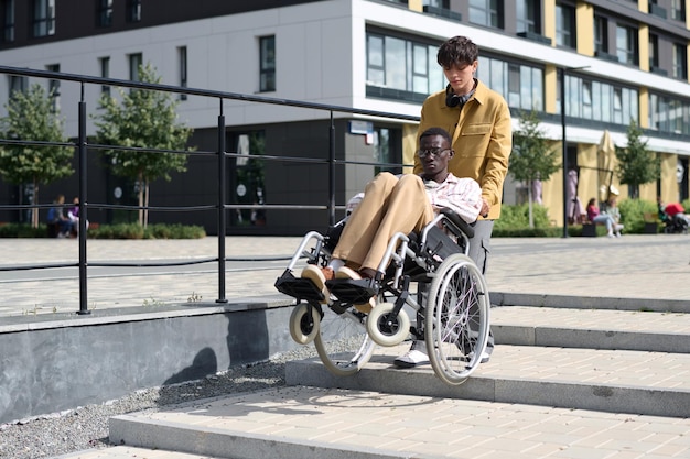 Homme aidant son ami en fauteuil roulant à descendre les escaliers lors de sa promenade en ville