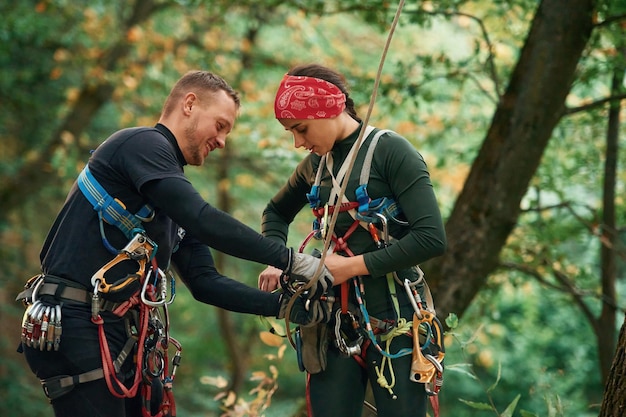 Photo l'homme aide la femme à grimper dans la forêt en utilisant un équipement de sécurité