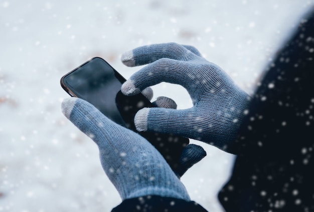 Homme à l'aide de smartphone en hiver avec des gants pour écrans tactiles