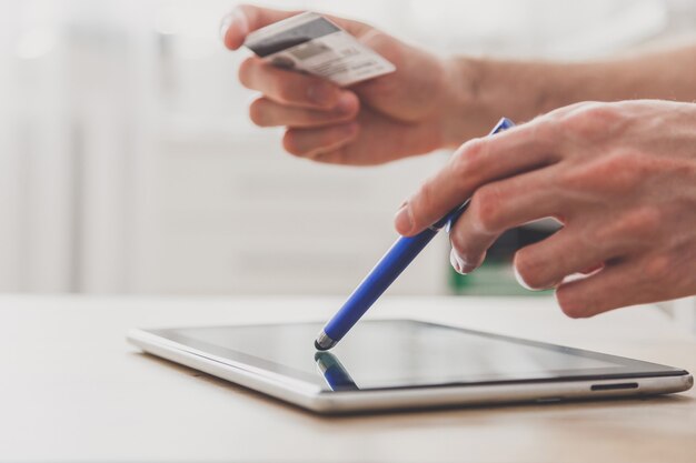 Homme à l'aide de tablette pc avec stylet et carte de crédit à la table, achats en ligne