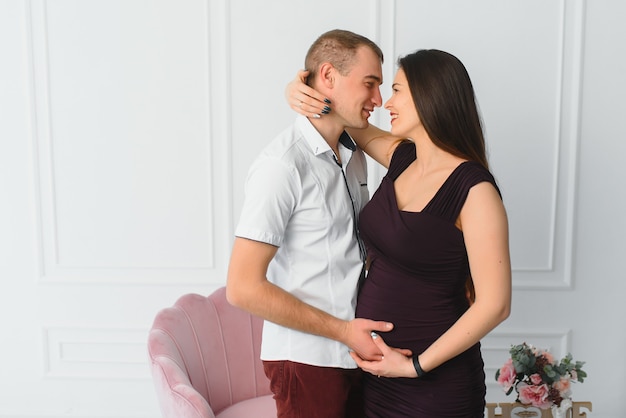 Homme aimant serrant sa femme enceinte par derrière debout près de la fenêtre à la maison, copiez l'espace