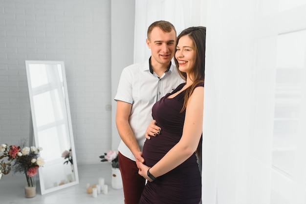 Homme aimant serrant sa femme enceinte par derrière debout près de la fenêtre à la maison, copiez l'espace