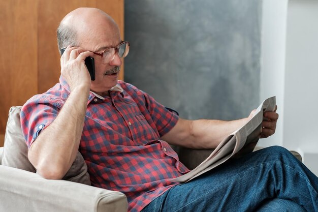 Homme aîné dans le salon lisant le journal parlant au téléphone avec ses enfants