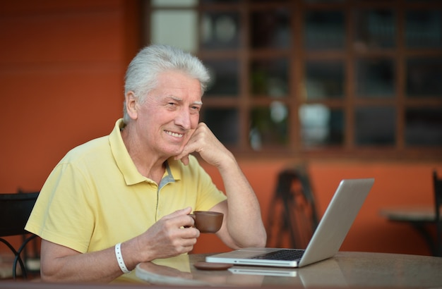 Homme aîné s'asseyant avec l'ordinateur portable et le café dans l'hôtel