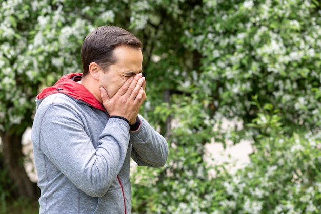 Un homme avec une allergie ou des éternuements froids contre un arbre en fleurs