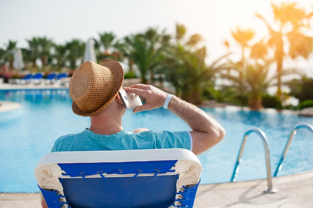 Homme allongé sur une chaise longue et parlant au téléphone près de la piscine