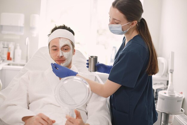 Homme allongé dans un cabinet d'esthéticienne avec un masque appliqué sur son visage