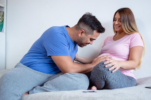 homme allongé dans son lit regardant et touchant sa femme enceinte ventre