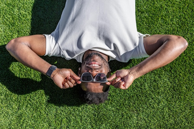 Un homme allongé sur l'herbe tenant des lunettes de soleil