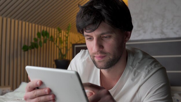 Homme allongé sur le lit à l'aide de tablette numérique.