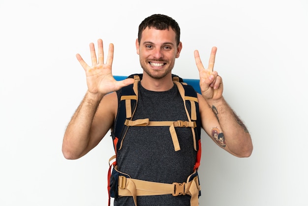Homme d'alpiniste brésilien avec un gros sac à dos sur fond blanc isolé comptant sept avec les doigts