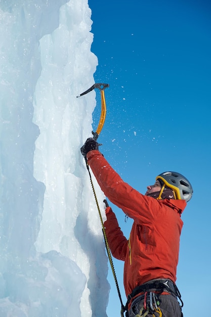 Homme alpiniste avec piolets hache escalade un grand mur de glace. Portrait de sports de plein air.