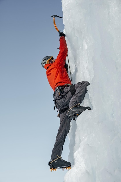 Homme alpiniste avec piolets hache escalade un grand mur de glace. Portrait de sports de plein air.