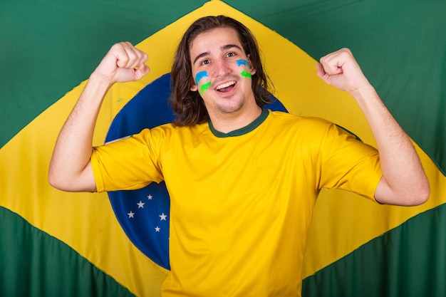Homme d'Amérique latine brésilien brésilien acclamant la coupe du monde du brésil 2022 vibrant et acclamant avec le fond du drapeau du brésil