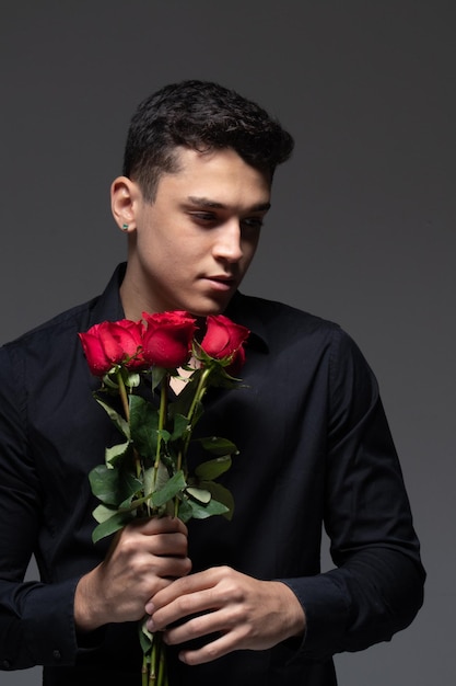 homme amoureux portant des vêtements sombres tenant un bouquet de roses rouges photo en studio fond gris