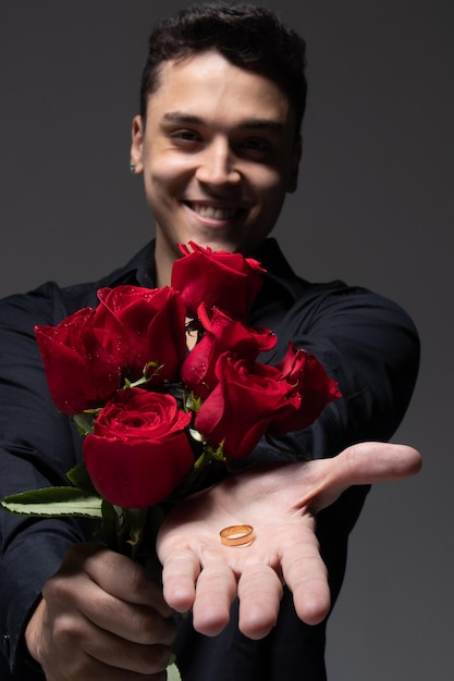 homme amoureux portant des vêtements sombres tenant un bouquet de roses rouges photo en studio fond gris