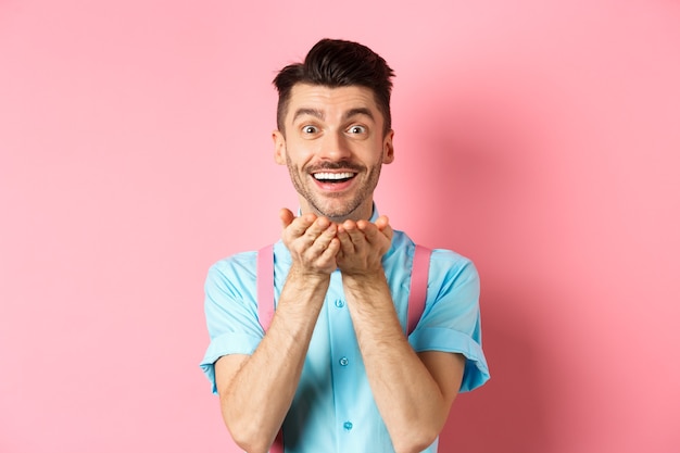 Homme amoureux soufflant baiser à la caméra et souriant passionné, regardant amant heureux, profitant de la Saint-Valentin, debout sur le rose.