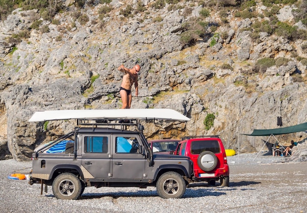 Un homme ancre le kayak sur une jeep sur une plage en Grèce